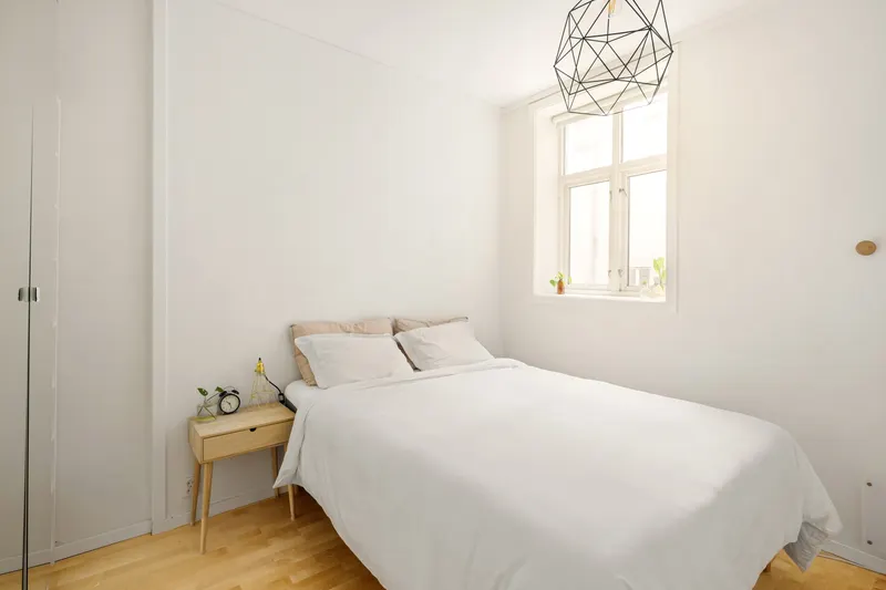 Dormitorio con cama blanca y suelo de madera